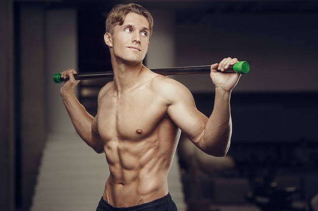 Hombre de fitness en el entrenamiento en el gimnasio con barra de estiramiento de los músculos