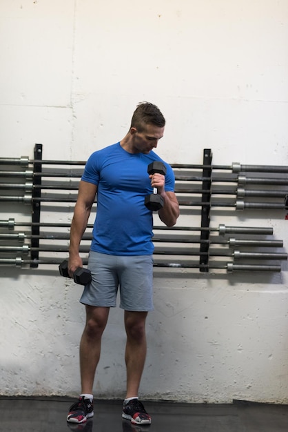 hombre de fitness de entrenamiento con pesas dentro de la elaboración de brazos levantando pesas haciendo flexiones de bíceps. Modelo deportivo masculino haciendo ejercicio en interiores como parte de un estilo de vida saludable.