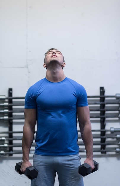 Foto hombre de fitness de entrenamiento con pesas dentro de la elaboración de brazos levantando pesas haciendo flexiones de bíceps. modelo deportivo masculino haciendo ejercicio en interiores como parte de un estilo de vida saludable.