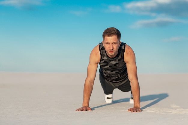 Hombre fitness haciendo ejercicios en el desierto de arena.