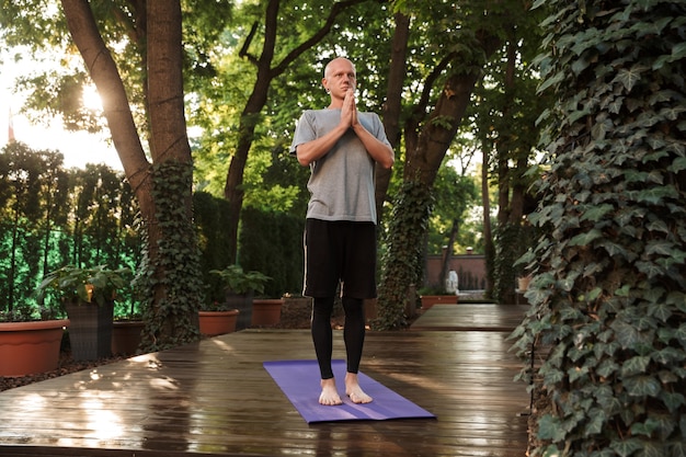 Hombre fitness joven concentrado haciendo ejercicios de yoga meditativos al aire libre en una estera de fitness