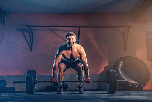 Hombre de fitness muscular haciendo empujar una barra sobre su cabeza en su garaje, autoaislamiento. Entrenamiento funcional. Ejercicio de arranque.