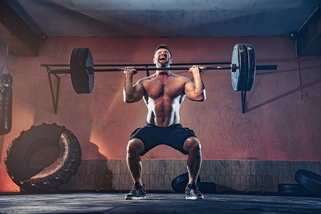 Hombre de fitness muscular haciendo empujar una barra sobre su cabeza en su garaje, autoaislamiento. Entrenamiento funcional. Ejercicio de arranque.