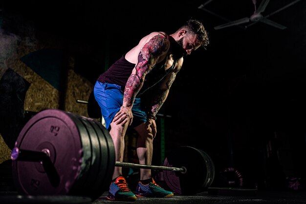 Hombre de fitness muscular que se prepara para hacer peso muerto con una barra en el moderno gimnasio.