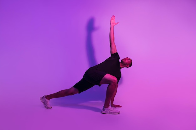 Hombre fitness negro practicando yoga sobre fondo de estudio púrpura