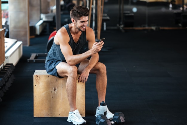 Hombre fitness se sienta en la caja con teléfono. sonriente