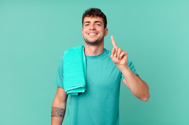 Foto hombre de fitness sonriendo y mirando amigable, mostrando el número uno o el primero con la mano hacia adelante, contando hacia atrás