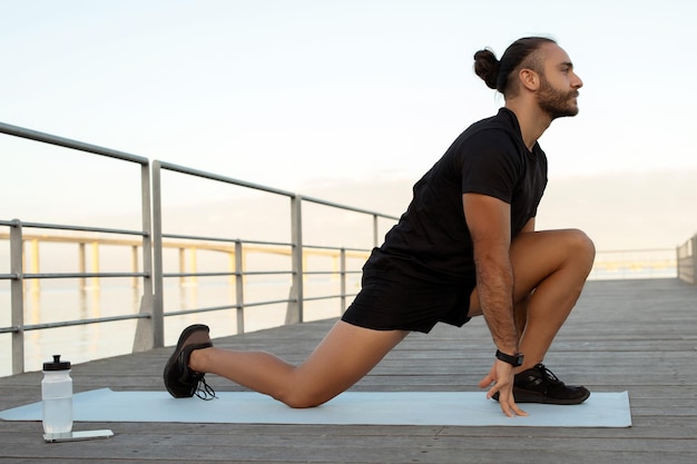 Hombre flexionando las piernas arrodillado haciendo ejercicio de estiramiento del flexor de la cadera al aire libre