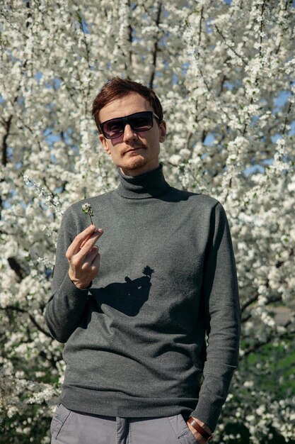 Hombre con flor blanca de pie en el jardín con árboles florecientes en un día soleado en primavera