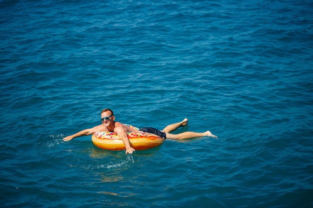 Un hombre flota sobre un anillo inflable en el mar con agua azul. Vacaciones en el mar en un día soleado. Concepto de vacaciones de Turquía