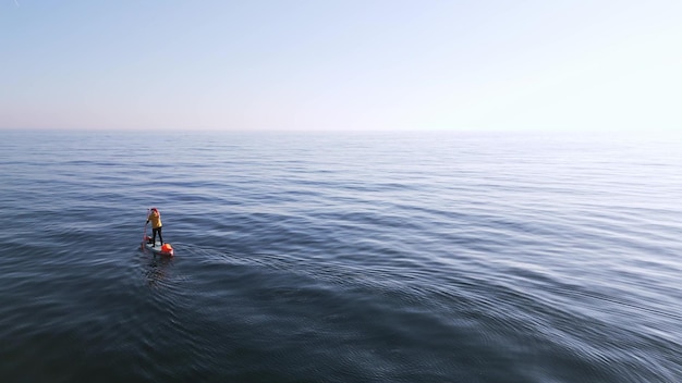 El hombre flota en el tablero de SUP en las tranquilas aguas azules claras de la vista aérea del Mar Negro