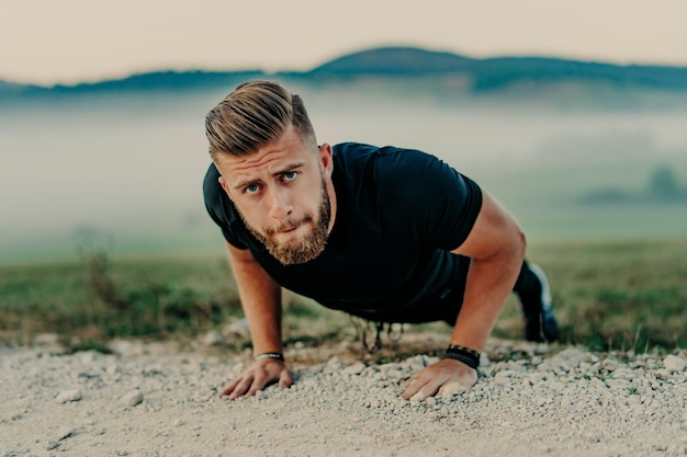 Un hombre en forma haciendo ejercicios de flexiones en el gimnasio al aire libre. Atleta de entrenamiento corporal central haciendo planchas o haciendo flexiones sobre el césped.