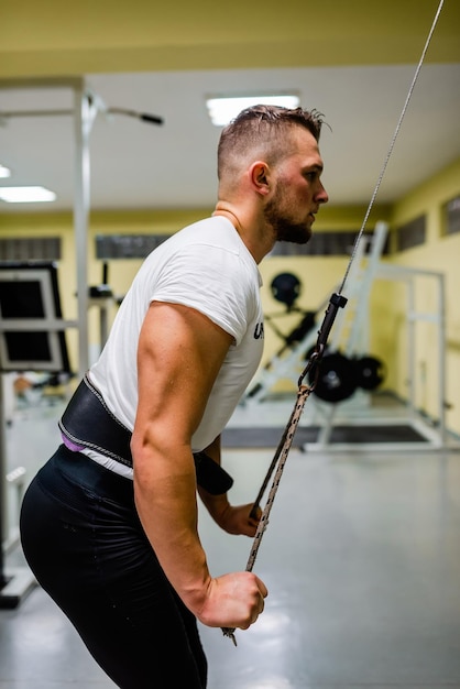 Un hombre en forma muscular haciendo ejercicio de tríceps con cable en el gimnasio