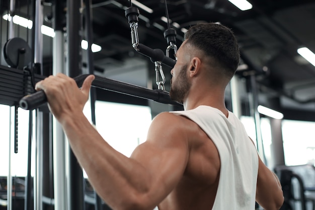 Hombre en forma y musculoso sacude la espalda en el simulador. Vista trasera.