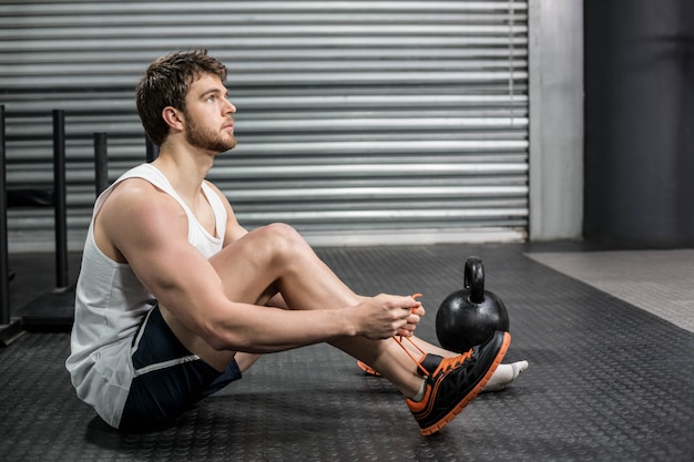 Hombre en forma que ata sus cordones de zapatos en el gimnasio