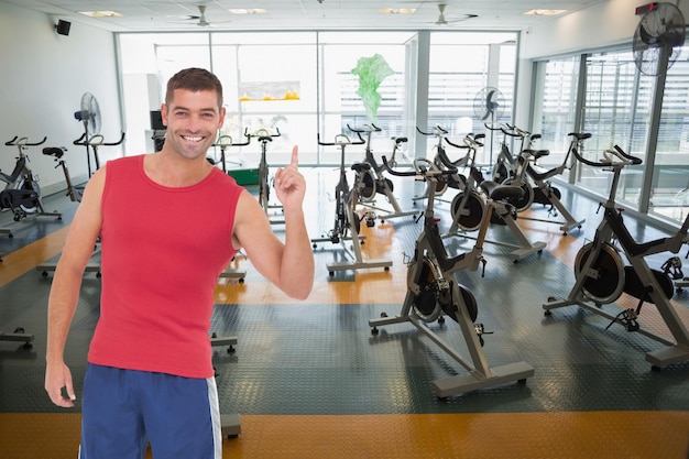 Un hombre en forma sonriendo y apuntando contra un gran estudio de fitness vacío con bicicletas giratorias