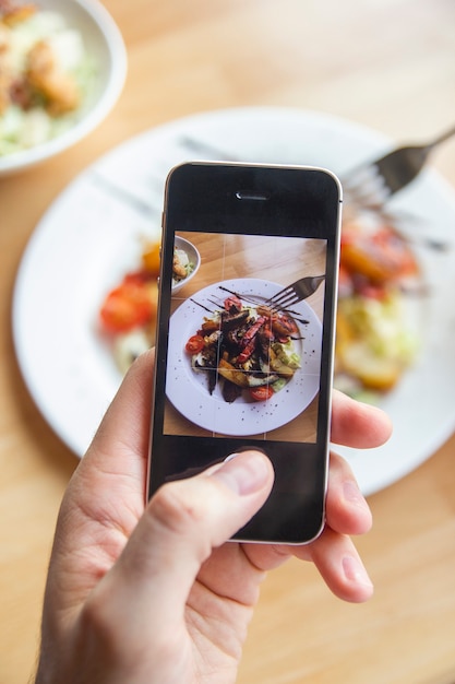 Foto un hombre fotografía una deliciosa ensalada en su teléfono en un restaurante