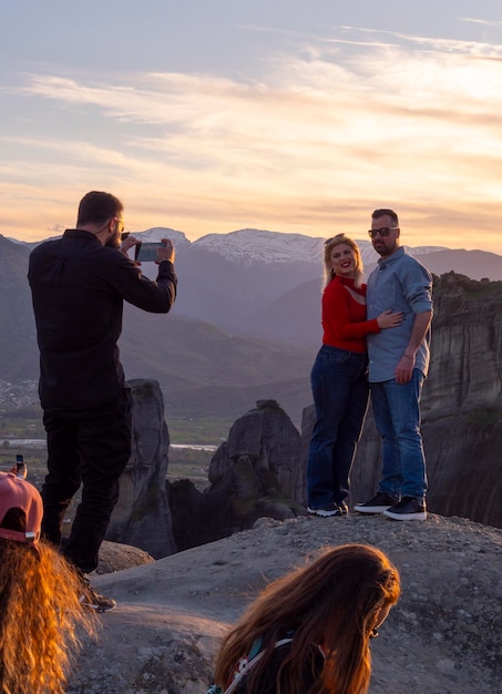 Un hombre fotografía a una joven pareja feliz en las montañas de Meteora en Grecia al atardecer