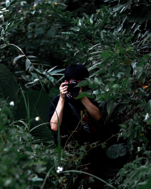 Foto hombre fotografiando con una cámara en medio de plantas