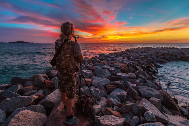 Foto hombre fotografiando mientras está de pie en las rocas en la playa contra el cielo durante la puesta de sol