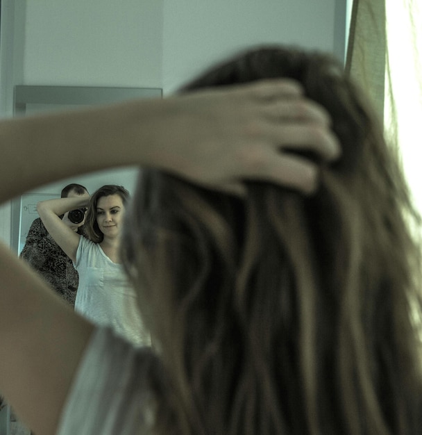 Foto hombre fotografiando a una mujer con la mano en el cabello mientras se refleja en el espejo en casa