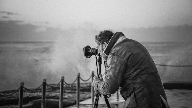 Hombre fotografiando las olas del mar a través de una cámara de trípode desde el paseo marítimo