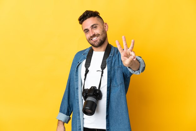 Hombre fotógrafo aislado en amarillo feliz y contando tres con los dedos