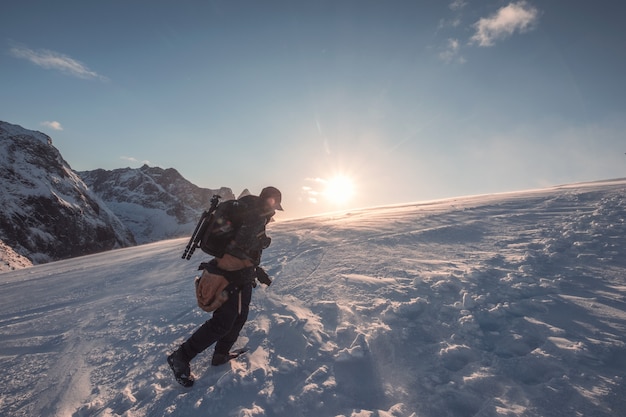 Hombre fotógrafo escalada en montaña nevada con cielo azul al atardecer