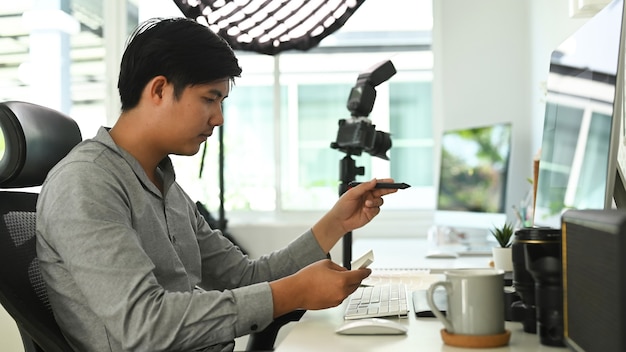 Un hombre fotógrafo independiente está trabajando en su proyecto en el escritorio de la oficina con varias computadoras.