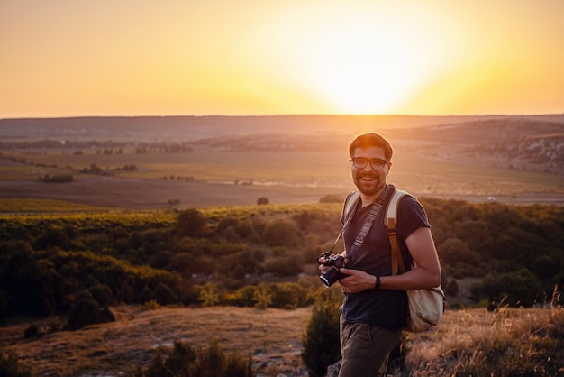 Hombre fotógrafo con mochila y cámara tomando fotos de las montañas al atardecer