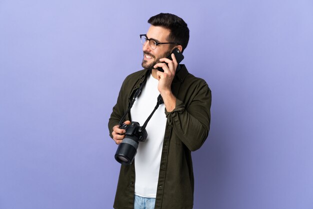 Foto hombre fotógrafo sobre pared púrpura aislado manteniendo una conversación con el teléfono móvil con alguien