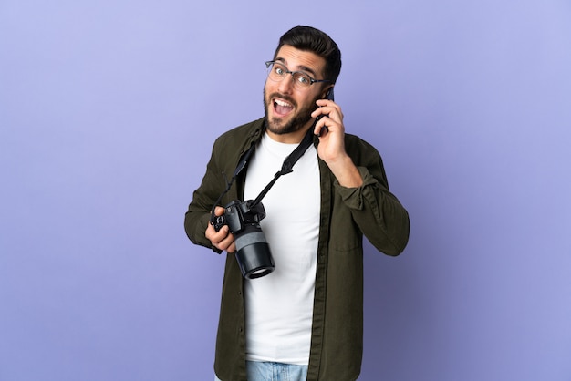 Hombre fotógrafo sobre pared púrpura aislado manteniendo una conversación con el teléfono móvil con alguien