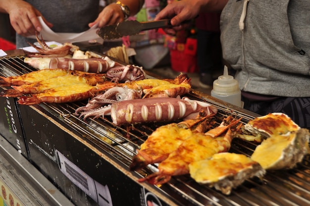 Hombre freír platos de mariscos a la barbacoa exóticos para la venta en la calle. Proveedor freír calamares en Hong Kong.