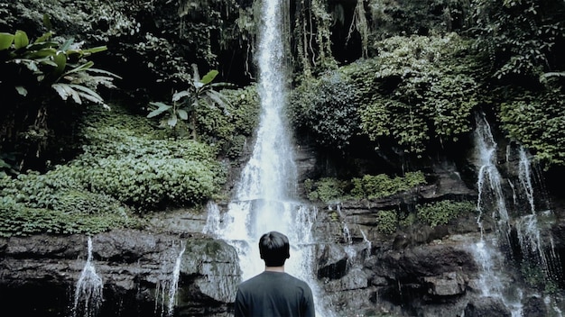 Foto un hombre se para frente a una cascada.