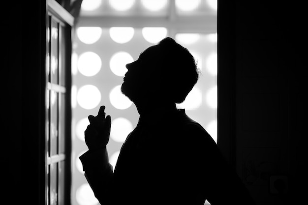 Un hombre se para frente a una ventana con una luz detrás de él.