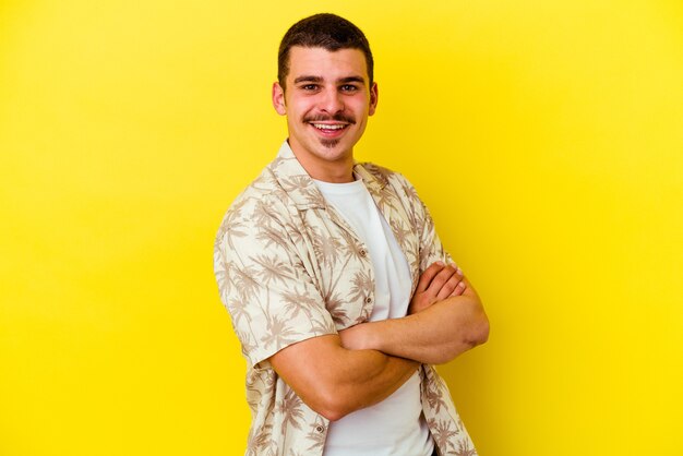 Hombre fresco caucásico joven aislado sobre fondo amarillo que se siente confiado, cruzando los brazos con determinación.