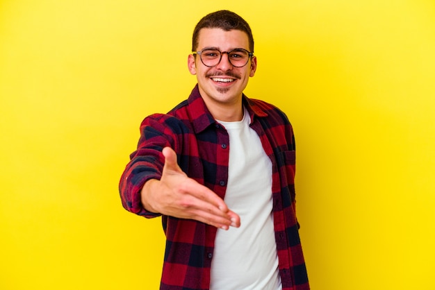 Hombre fresco caucásico joven en amarillo estirando la mano en gesto de saludo.