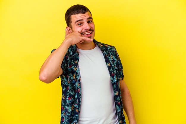 Hombre fresco caucásico joven en amarillo que muestra un gesto de llamada de teléfono móvil con los dedos.