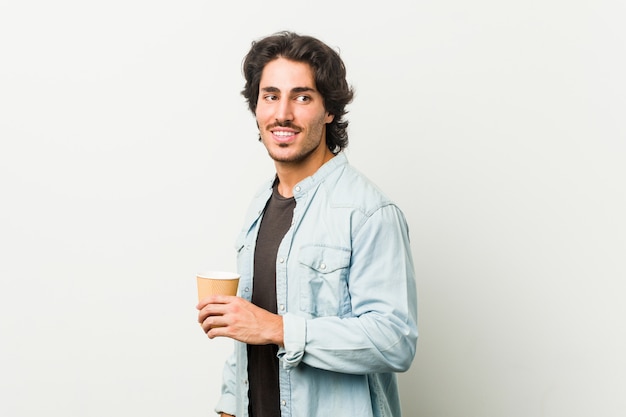 El hombre fresco joven que bebe un café mira a un lado sonriente, alegre y agradable.