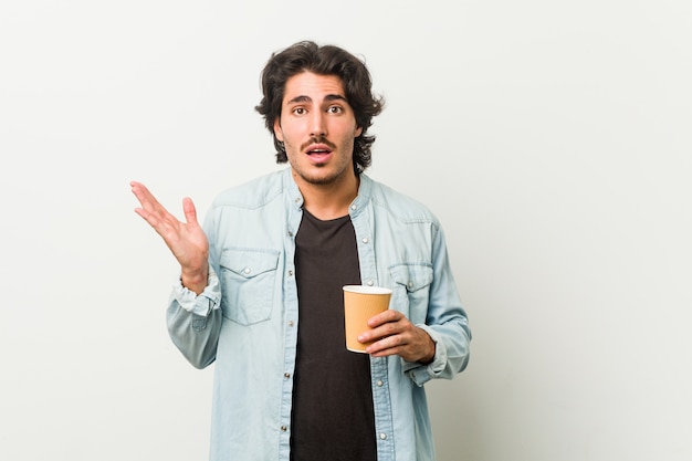 Hombre fresco joven que bebe un café sorprendido y conmocionado.