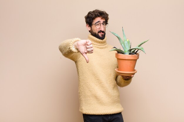 Hombre fresco joven que sostiene una planta de cactus contra la pared plana