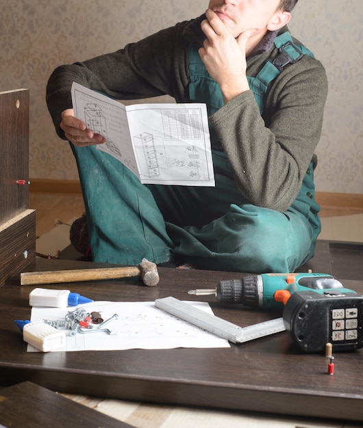 Hombre frustrado leyendo instrucciones y armando muebles de autoensamblaje DIY nuevo hogar y concepto de mudanza