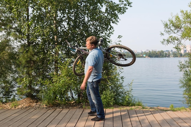 Foto hombre frustrado en el parque lleva una bicicleta rota en su hombro