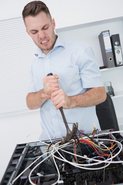 Hombre frustrado que usa el martillo para sacar los cables de la CPU