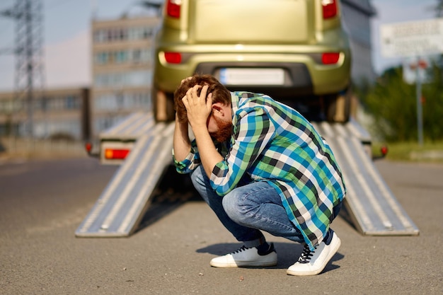 El hombre frustrado tiene un problema con el coche. Guy siente estrés mientras la grúa lleva su coche al taller de reparación de automóviles