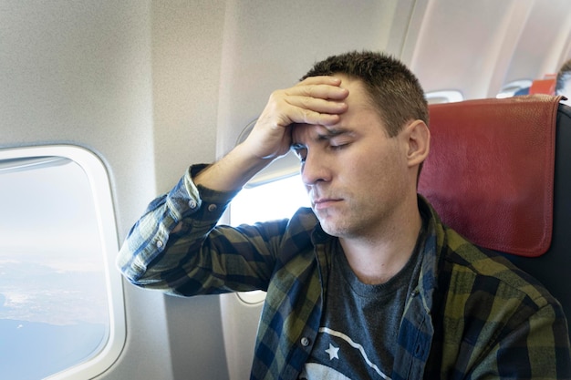 Foto hombre frustrado tocándose la cabeza con las manos y manteniendo los ojos cerrados mientras está sentado en su asiento airpla ...