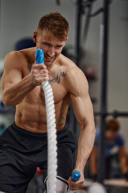 Hombre fuerte y agresivo musculoso entrenando con cuerda en el gimnasio de entrenamiento funcional Desenfoque de movimiento