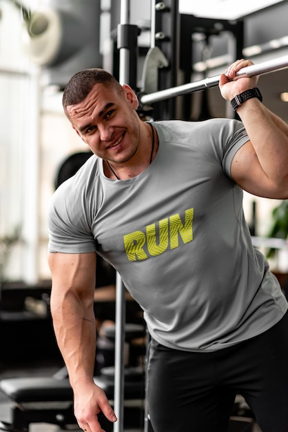 Un hombre fuerte y alegre va al gimnasio sacude los músculos de sus brazos y la espalda hace ejercicios de un joven atleta en un gran gimnasio