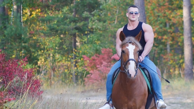 Un hombre fuerte con un cuerpo poderoso con una camiseta negra con gafas de sol monta un caballo