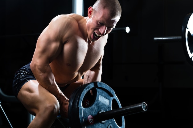 Hombre fuerte - culturista con pesas en un gimnasio, haciendo ejercicio con una barra